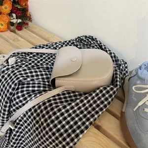 Detailansicht der minimalistischen beige Umhängetasche auf kariertem Stoff und Holzbank.