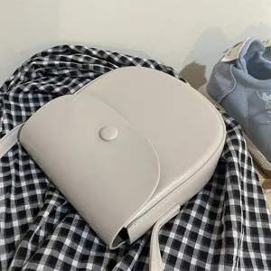 Detailansicht der eleganten minimalistischen beigen Umhängetasche auf kariertem Stoff.