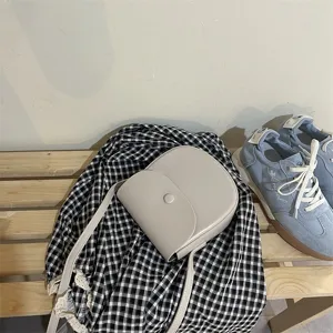 Detailaufnahme der hellgrauen minimalistischen Umhängetasche auf Karostoff mit Schuhen.