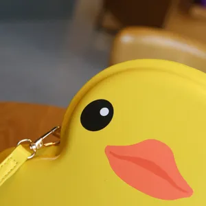 Close-up detail of cute yellow duck shaped crossbody bag with black eye and pink beak design.