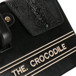 Detailed view of black crocodile pattern water bottle bag embroidery text hardware snap