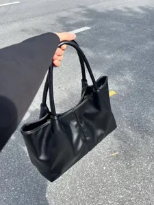 Detail view of a black leather tote bag with large capacity, showing texture and dual handles.