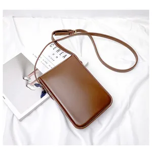 Detail view of minimalist brown vertical phone crossbody bag resting on clean white fabric.