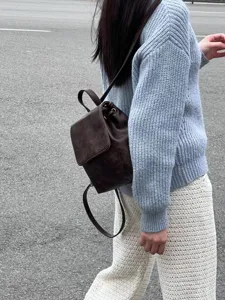 Dettaglio di un mini zaino marrone rétro abbinato a maglione blu, stile casual.