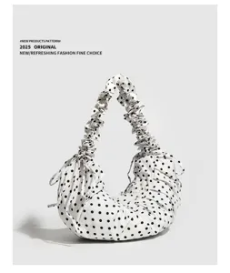 Detailed view of white polka dot canvas shoulder bag with ruffled strap and drawstring closure.