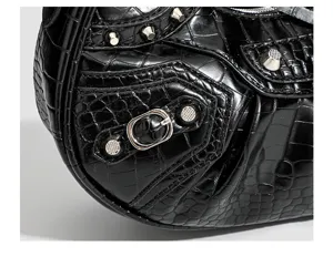 Detail view of black crocodile embossed motorcycle shoulder bag with silver studs and buckles.