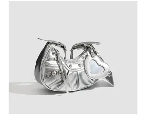 Silver metallic crescent shoulder bag detail, featuring metal studs and heart mirror charm.