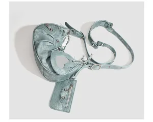 Detailed view of trendy blue leather crescent shoulder bag with metal studs and heart mirror.