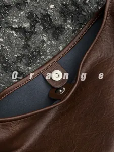 Brown leather tote bag detail close up showing magnetic snap closure and fine stitching.