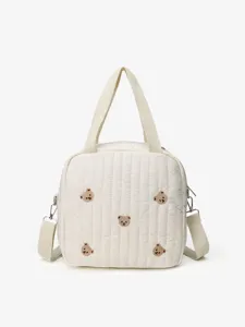 Close-up detail of cute embroidered bear pattern and quilted fabric on the soft cream tote bag.