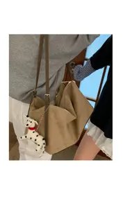 Detail shot of the casual suede shoulder pillow bag worn on shoulder with a cute plush dog pendant.