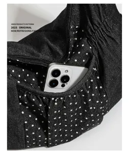 Vista dettagliata della tasca della borsa a tracolla in denim nero a pois con smartphone.