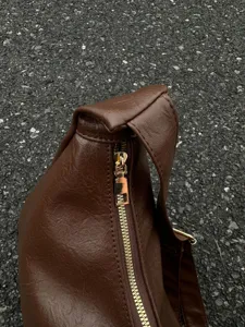Detail view of the brown leather shoulder bag featuring smooth zipper closure and gold hardware.
