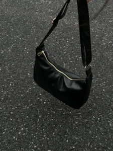 Detailed view of black minimalist hobo shoulder bag with gold tone zipper and adjustable strap.