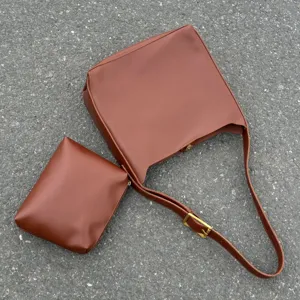 Detailed view of the brown slouchy hobo shoulder bag with matching pouch on textured ground.
