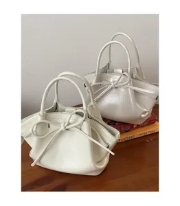 Primo piano di eleganti borse a secchiello bianche lucide con graziosi fiocchi e doppi manici.