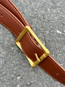 Close-up detail of a classic brown leather belt with a stylish vintage brass metal square buckle.