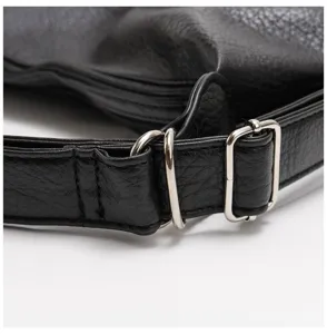 Dettaglio cinturino borsa in pelle nera primo piano con fibbie in metallo argentato.