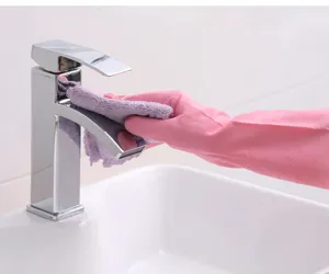 Detail view of pink rubber household cleaning gloves wiping a modern chrome faucet surface.