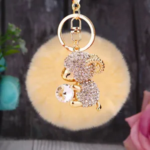 Plush pompom sheep keychain detail, cute crystal holding animal bag charm, gold keyring accessory.