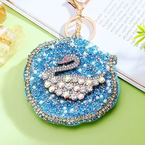Close-up of sparkling rhinestone swan compact mirror keychain with blue gems and gold hardware.