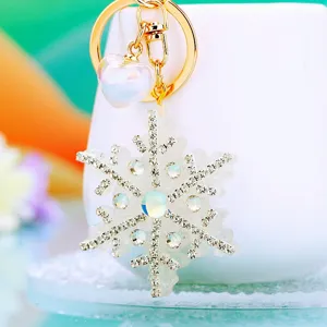 Close-up detail of rhinestone snowflake keychain pendant with heart charm and gold metal ring.