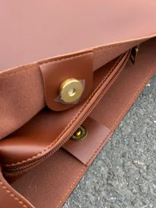 Close-up of brown leather handbag interior, showing golden magnetic snap and zipper.