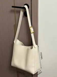 Detail view of a minimalist white slouchy shoulder handbag with gold hardware and size.