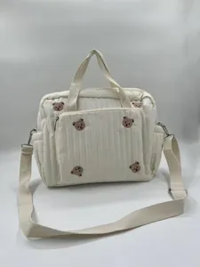Detail view of white quilted diaper bag with cute bear embroidery, dual handles and strap.