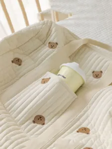 Quilted baby stroller bag detail, cute bear embroidery, soft beige diaper bag storage.