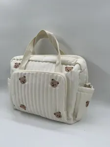 Quilted diaper bag with cute bear embroidery, multi-pocket design, white tote accessory detail.