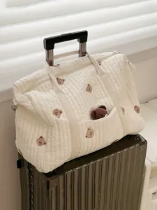 Quilted diaper bag detail view, cute bear embroidery and storage pocket, soft fabric.