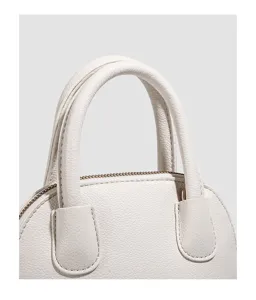 Close-up detail of white leather handbag handle and zipper, minimalist shell bag design.