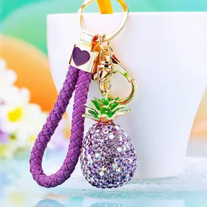Closeup detail of a sparkling rhinestone pineapple keychain, purple braided strap, cute bag charm.