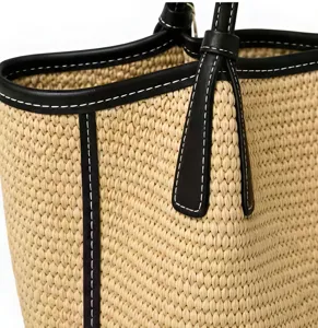 Nahaufnahme einer gewebten Strohtasche mit schwarzem Lederbesatz und weißen Nähten.