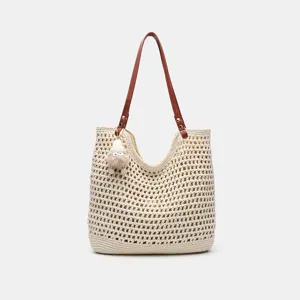 Detailansicht der gewebten Strohtasche mit braunen Henkeln und süßem Plüschanhänger.