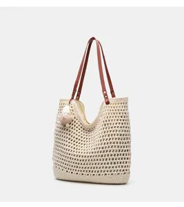 Geflochtene Stroh Shopper Tasche Detail mit Lochmuster braunen Lederriemen und süßem Plüschanhänger.
