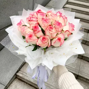 Bouquet de roses rose et blanc emballé dans du papier cadeau blanc avec des étoiles