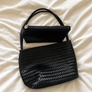 Black woven leather handbag detailed view, classic woven texture shoulder underarm bag style.