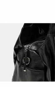 Detailansicht des Reißverschlusses einer schwarzen Ledertasche mit Metallring und Band.