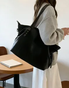 Vista detallada del bolso tote negro de cuero suave llevado al hombro con tachuelas.