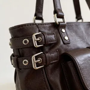 Λεπτομέρεια από καφέ ρετρό τσάντα με μεταλλικές αγκράφες και υφή δέρματος υψηλής ποιότητας.
