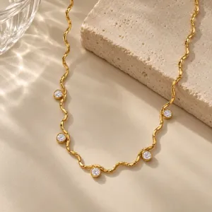 Gros plan d'un collier en acier titane doré ondulé serti de pierres de zircon rondes scintillantes.