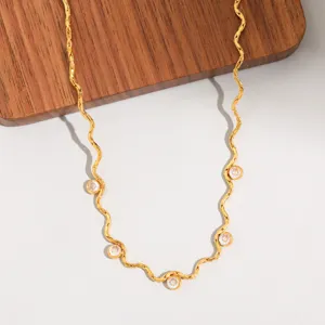 Gros plan détaillé du collier en acier titane doré ondulé avec des pierres scintillantes.