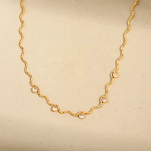 Détail en gros plan du collier en acier titane doré ondulé avec des pierres de zircone étincelantes.