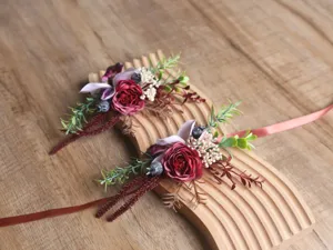 Detailansicht der wald-retro Hochzeitsboutonnieres mit burgunderroten Rosen und Blättern.