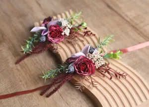 Vintage Hochzeits-Boutonnieres im waldigen Stil mit burgunderroten Rosen und gruenen Blaettern.