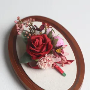 Nahaufnahme des künstlichen roten Rosen-Ansteckblümchens mit rosa Blüten und grünen Blättern.