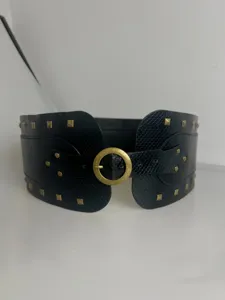 Detailopname van brede zwarte korsetriem met krokodillenstructuur en gouden ronde gesp.
