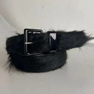Primer plano detalle de un cinturón de pelo negro con hebilla cuadrada negra brillante.